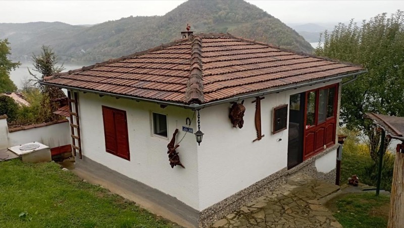 Okrečena bela kuća s crepom i crvenim kapcima, iza nje Dunav i brda Đerdapa